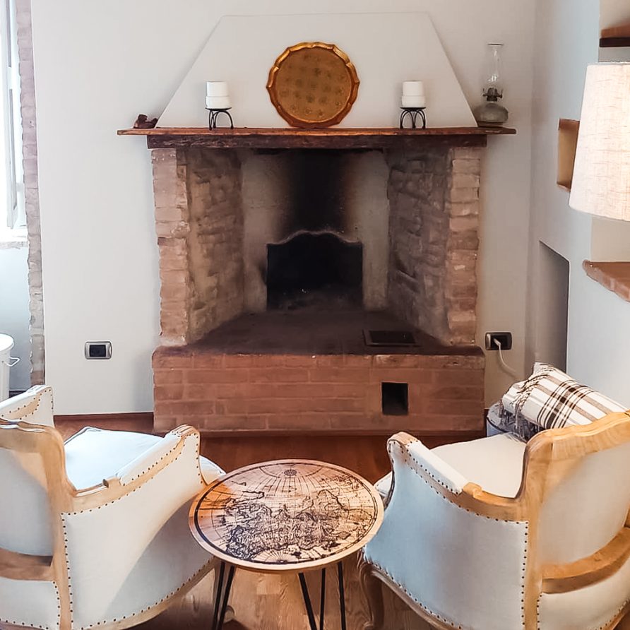 Interior of renovated holiday apartment in Suvereto Tuscany Italy showing exposed brick fireplace and two ornate armchairs